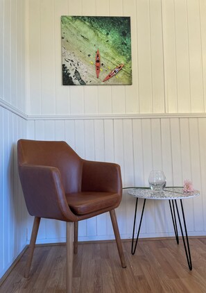 A cozy room with a leather chair, framed artwork, and a small table with a single flower.