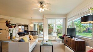 A modern living room with a white sofa, glass coffee table, and a TV on a wooden cabinet. - Light and Airy North Shore Condo. Owner hosted w/on site Co-host!  (Princeville)