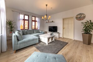 Een moderne woonkamer met een grijze bank, een witte salontafel, een televisie en een grote plant.