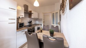 Et moderne køkken med hvide skabe, en træbordplade og et spisebord med stole. En hængende lampe er placeret over køkkenbordet.