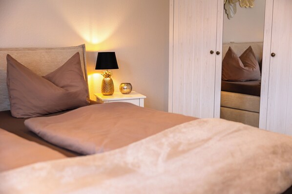 A neatly made bed with a headboard, a bedside lamp, and a nightstand with a decorative pineapple and a small bowl.