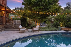 A swimming pool with a tiled edge, surrounded by a wooden deck and outdoor seating.