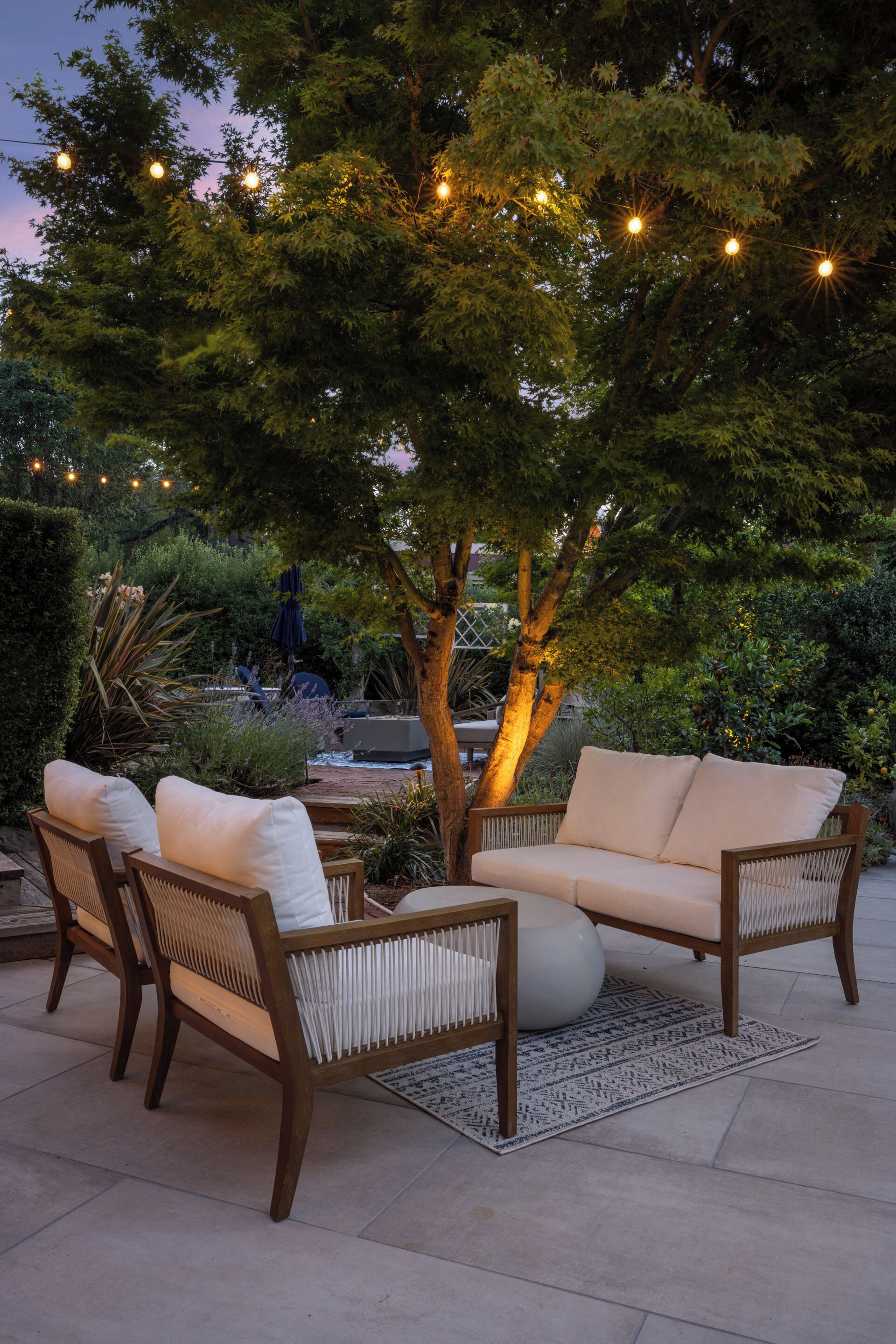 An outdoor seating area with wicker furniture, a round table, and string lights.
