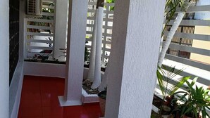 A covered outdoor area with white pillars, red flooring, and potted plants. - Posada tulys place (San Andrés)