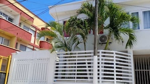 A residential building with a white gate, a palm tree, and a red and yellow facade. - Posada tulys place (San Andrés)