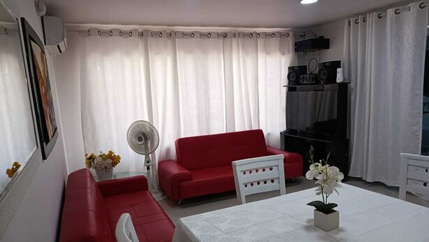 A living room with a red sofa, white chairs, a dining table with a white tablecloth, and a fan. - Posada tulys place (San Andrés)