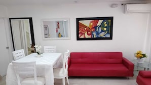A dining area with a white table and chairs, a red sofa, and a colorful butterfly painting on the wall. - Posada tulys place (San Andrés)