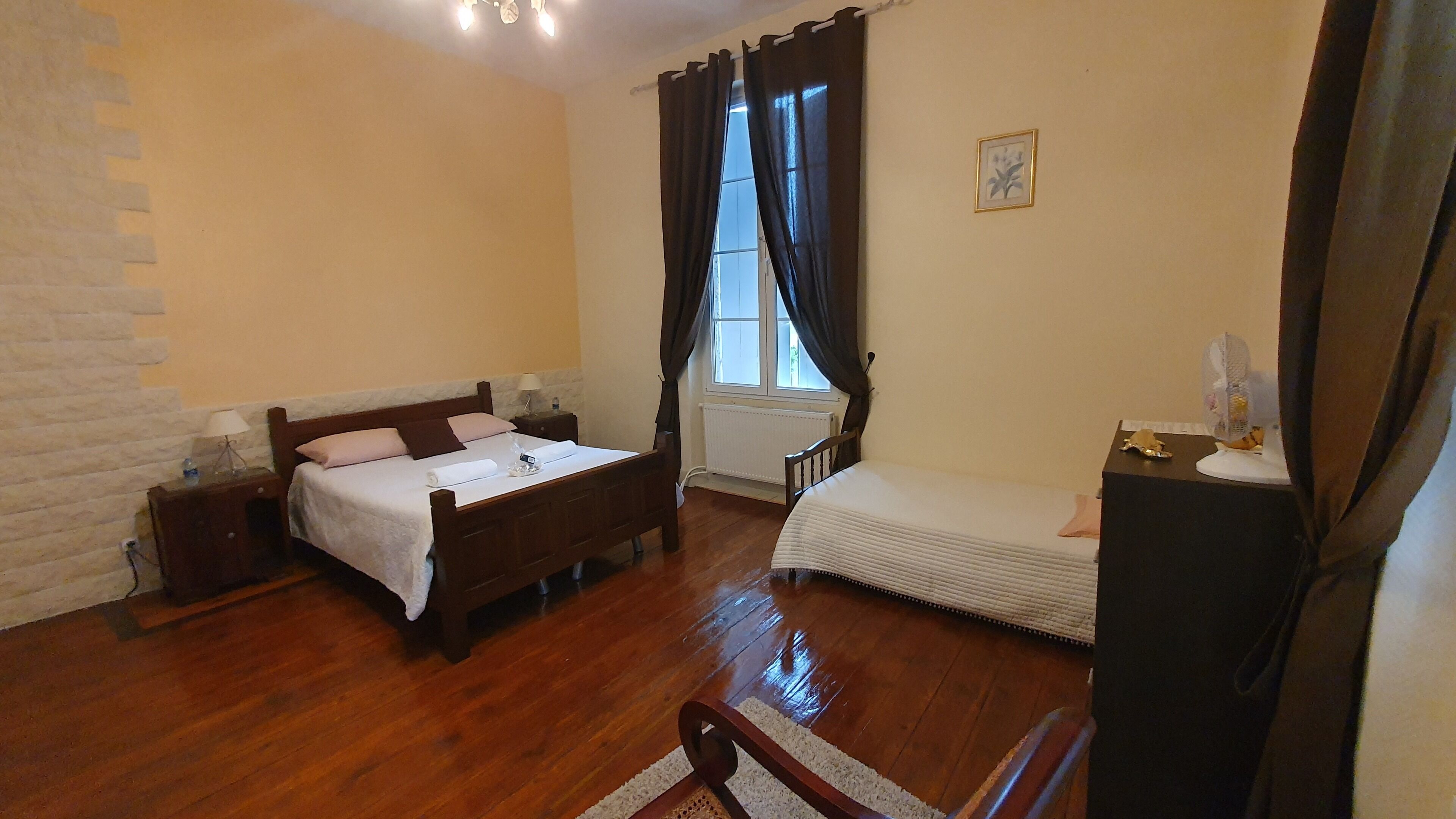 A room with a wooden bed, a small bedside table, a chair, a radiator, and a window with curtains.