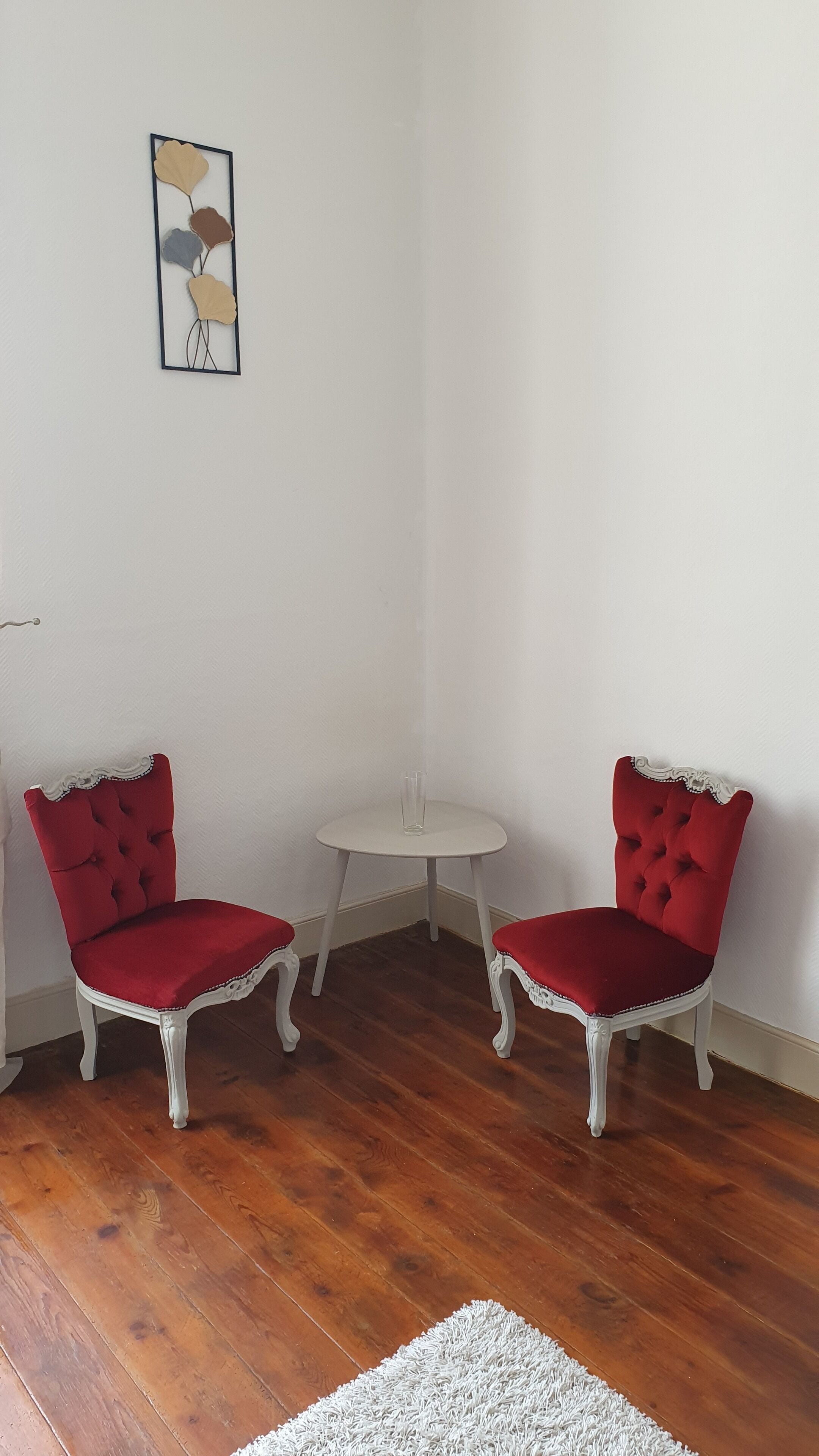 Une pièce d’angle avec deux fauteuils rouges, une petite table ronde et un tapis blanc.