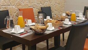 A breakfast setup with a stone wall, a whiteboard with utensils, and a table with breakfast items. - Domaine De l Ourbise  (Razimet)