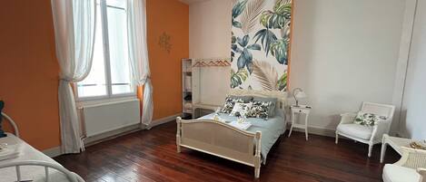 A bedroom with a bed, a chair, a small table, and a large window with curtains.