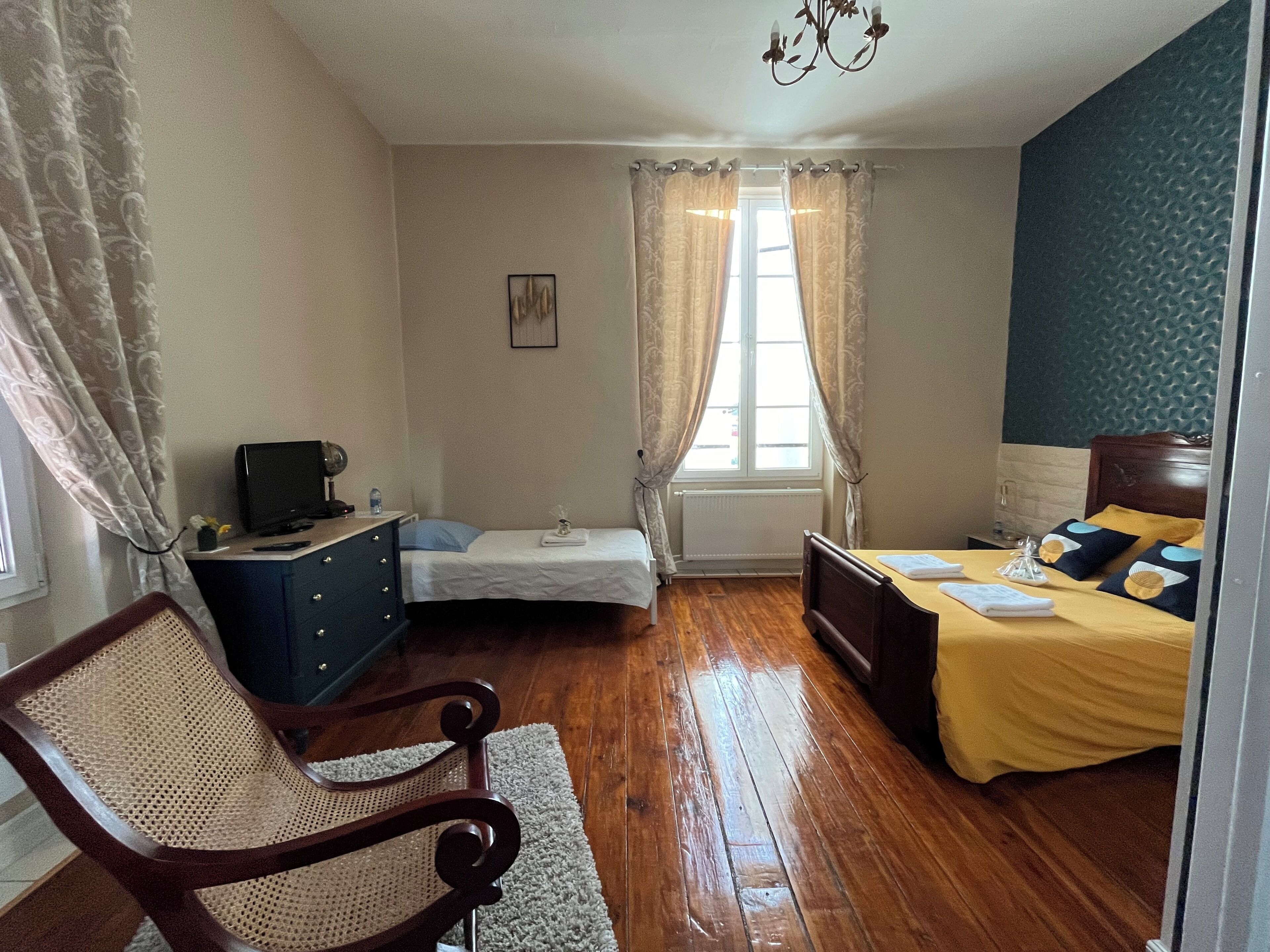 A room with a wooden floor, a bed with a yellow bedspread, a desk with a computer, a chair, and a window with curtains.