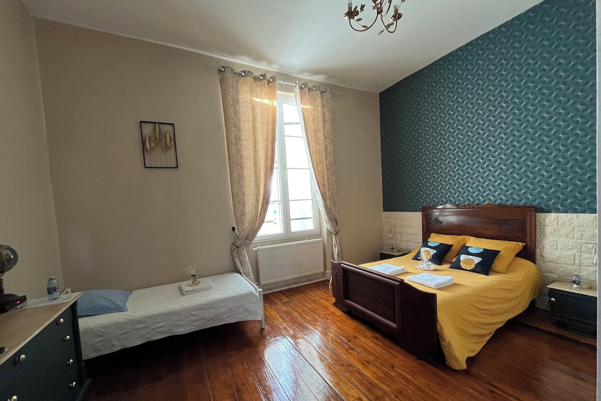 Um quarto com cama, uma mesa pequena, uma cadeira e uma janela com cortinas.