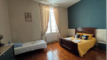 Un dormitorio con cama, una mesita, una silla y una ventana con cortinas.