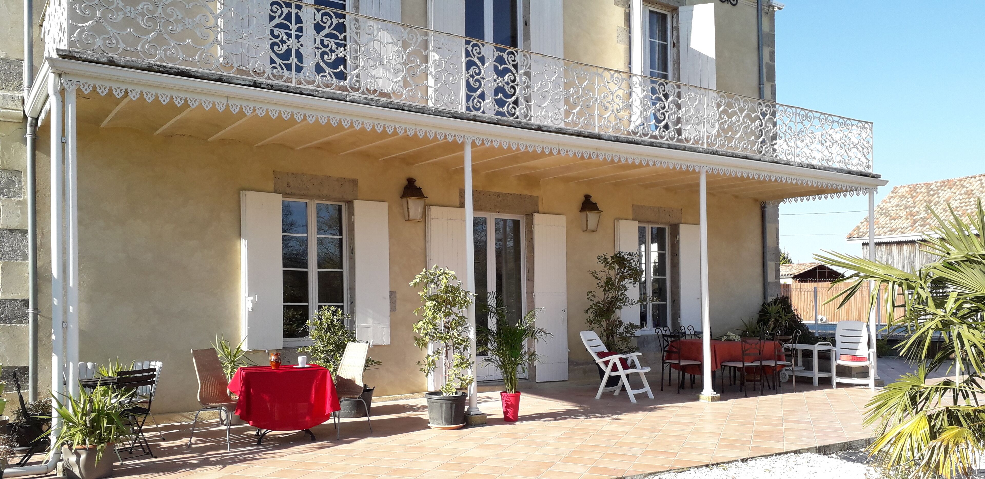 A covered outdoor patio with a balcony, potted plants, and outdoor seating.