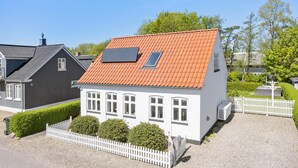 Ein zweistöckiges Haus mit rotem Ziegeldach, weißen Außenwänden und einem kleinen Fenster im zweiten Stock.
