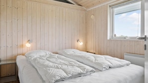 Et værelse med træpaneler, en seng med hvidt sengetøj, to vægmonterede lamper og et vindue med udsigt til himlen.