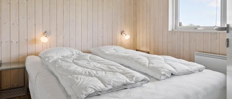 Ein Zimmer mit Holzwandverkleidung, einem Bett mit weißer Bettwäsche, zwei Wandlampen und einem Fenster mit Blick zum Himmel.