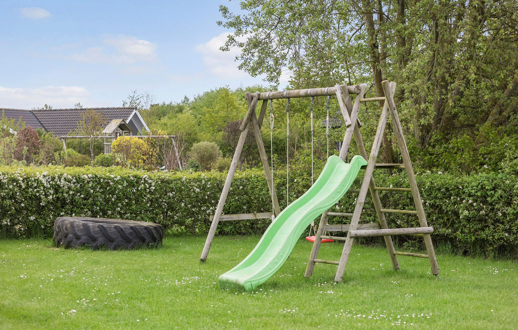 A wooden swing set with a green slide in a grassy yard with a house in the background.