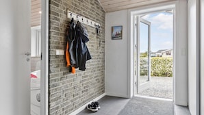 En gang med en murstensvæg, et knagered med jakker, en dør der fører ud, og en lille dør med et skohold.