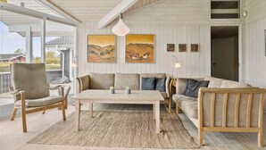 En hyggelig stue med sofa, stole, et bord og billedkunst på væggen.