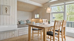 Et hyggeligt interiør med træbord, stole, bænk med puder, et lille vindue og en hængende lampe.