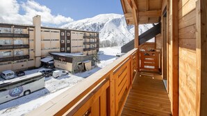 Un balcon en bois offrant une vue sur une montagne enneigée et sur un immeuble à plusieurs étages.