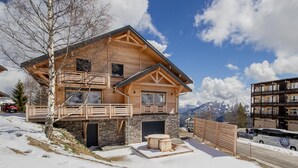 Un chalet en bois avec des fondations en pierre, un balcon et une cheminée en pierre.