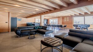 Un espace intérieur vaste et lumineux, avec des poutres en bois, un canapé en cuir noir et une table à manger.
