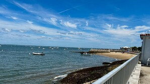A coastal scene with boats on the water, a sandy beach, and a pier with buildings. - Magnificent T3 with panoramic seafront view (Arcachon)