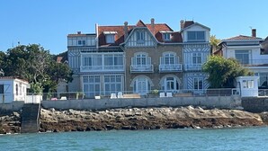 A waterfront property with a multi-story building featuring balconies, a stone retaining wall, and a clear view of the water. - Magnificent T3 with panoramic seafront view (Arcachon)