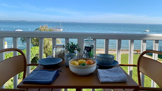 A table with a bowl of fruit, a jar labeled "TEA", and a blue bowl on a balcony overlooking the sea. - Magnificent T3 with panoramic seafront view (Arcachon)