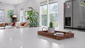 A modern kitchen with white cabinetry, a stainless steel refrigerator, and a large island with a tray and potted plant. - Stylish Chattanooga Retreat Minutes to Downtown (Chattanooga)