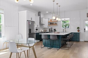 Une cuisine moderne avec des meubles blancs, un îlot central doté de tabourets et des luminaires suspendus.