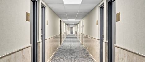 Passadís d'hotel amb una catifa estampada, portes numerades i una làmpada al sostre.