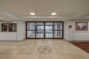A hotel lobby with a large entrance, tiled flooring, and a framed artwork on the wall.