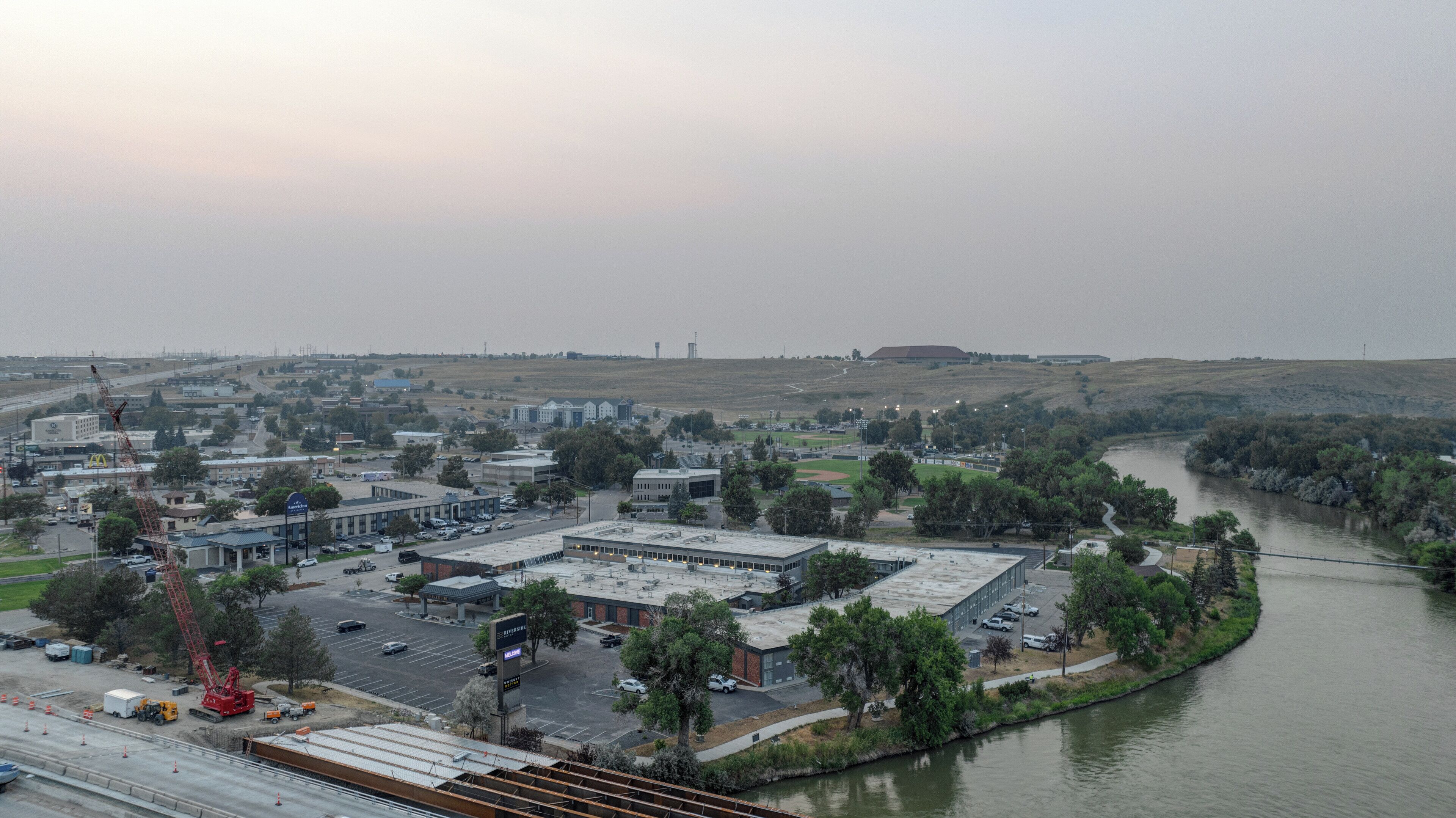 A riverside view of a commercial area with buildings, a parking lot, and a construction crane.