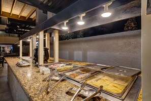 A buffet area with various food options, including French fries and fried items, in a modern setting with granite countertops and overhead lighting.