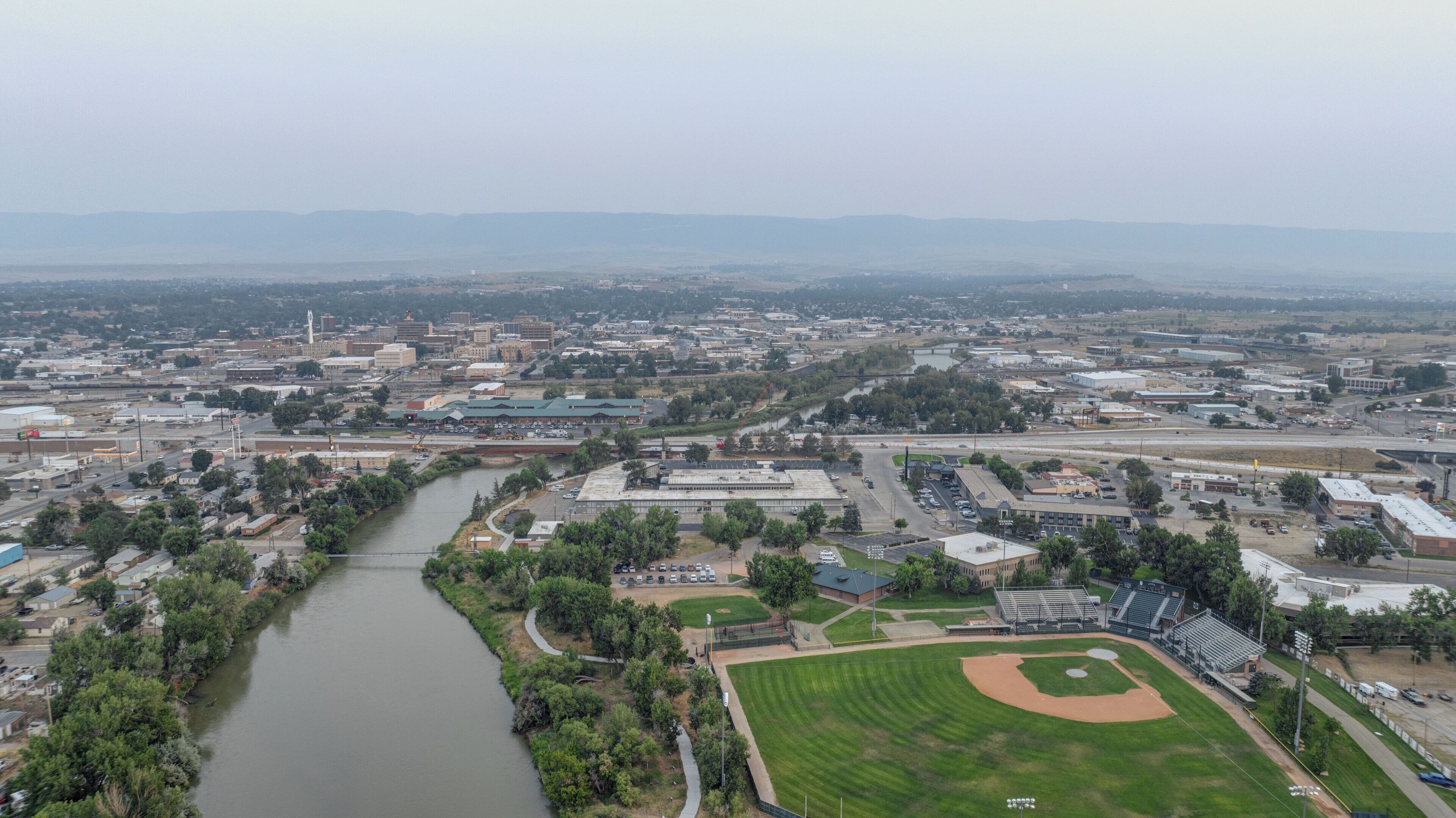 An aerial view of a city with a river, baseball field, and industrial buildings.