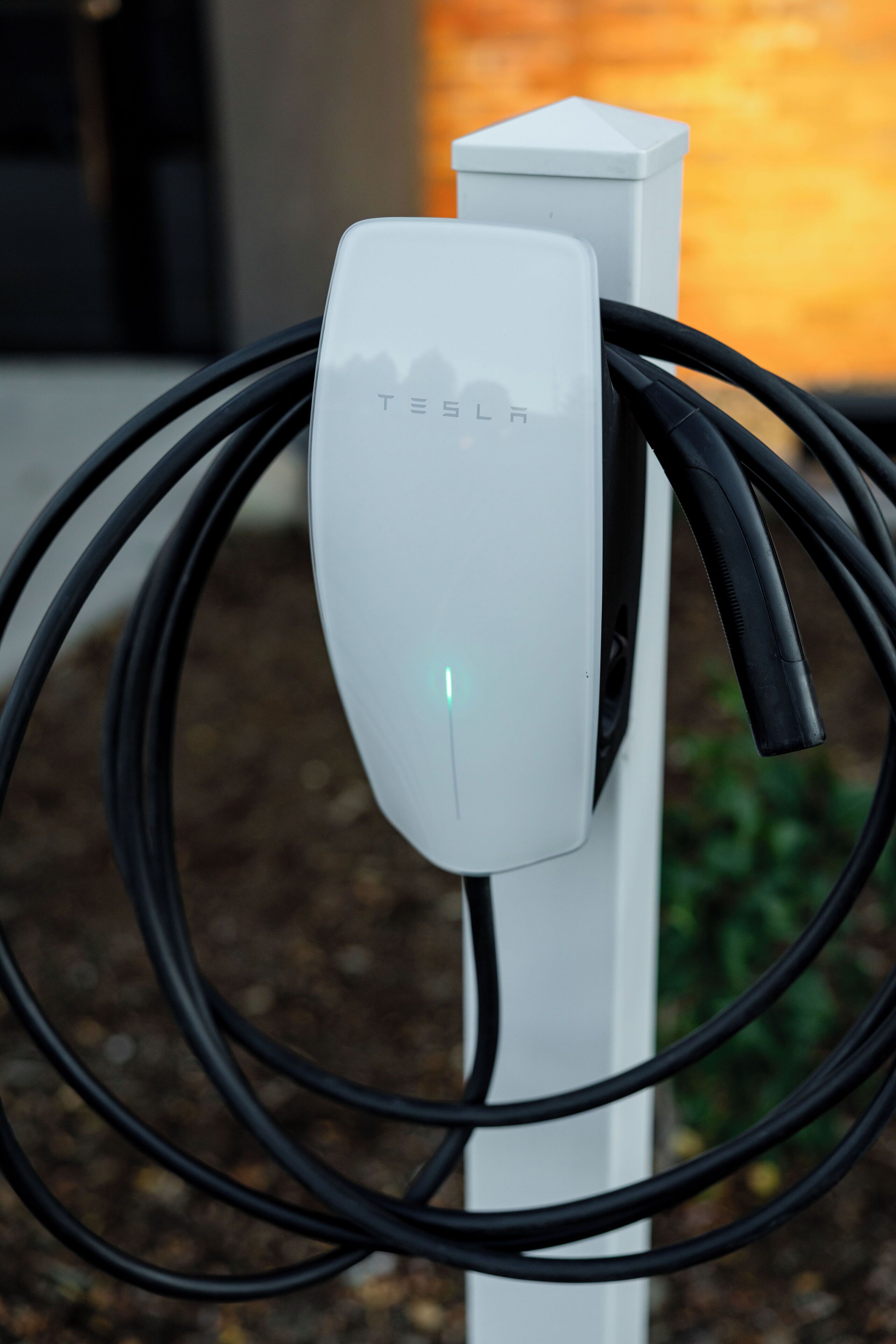 A Tesla charging station with a white charging unit and black cables.