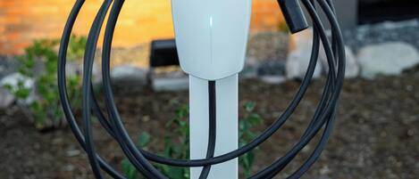 A white electric vehicle charging station with a brick wall and a modern building in the background.