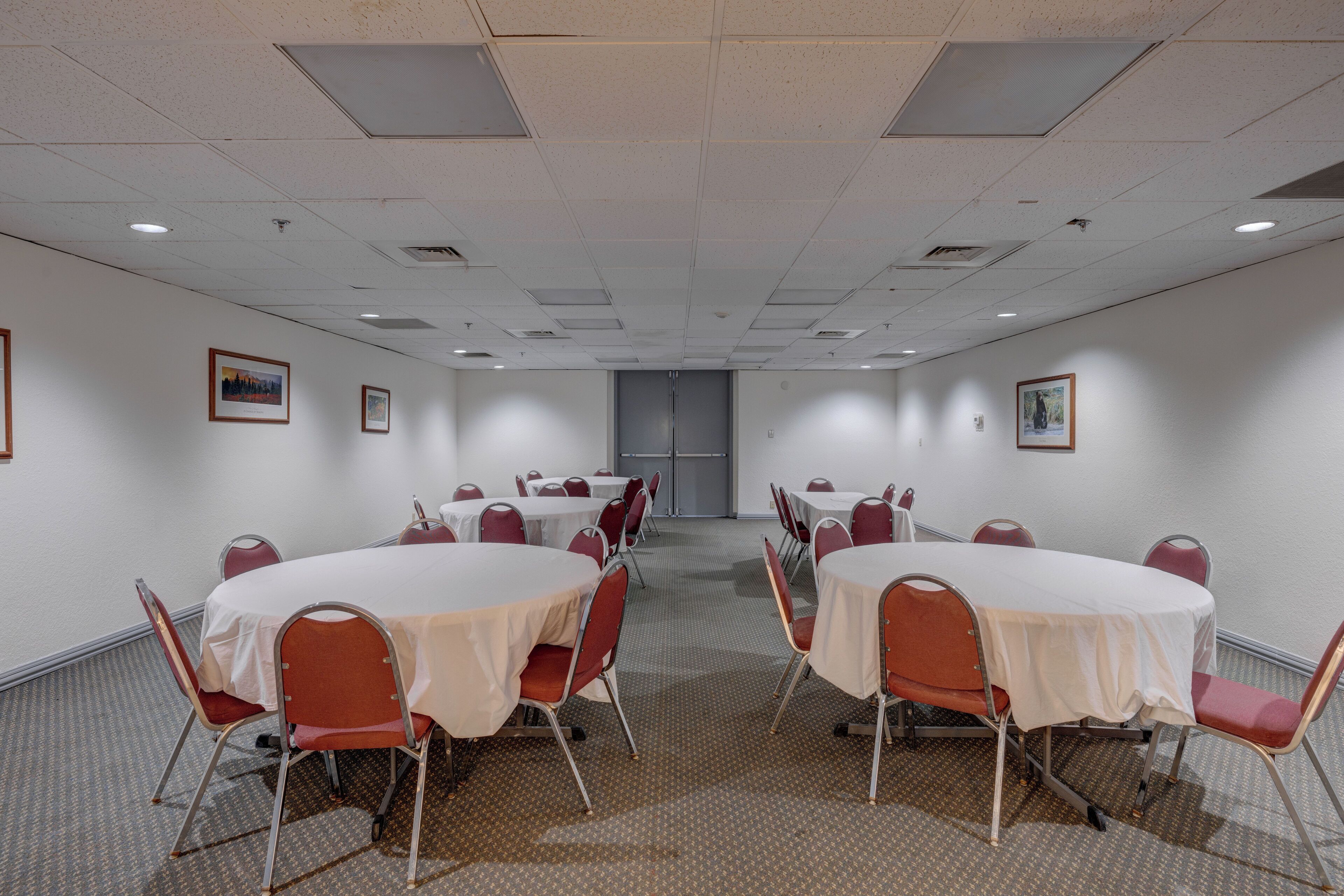 A conference room with round tables and red chairs, white walls, and framed pictures on the walls.