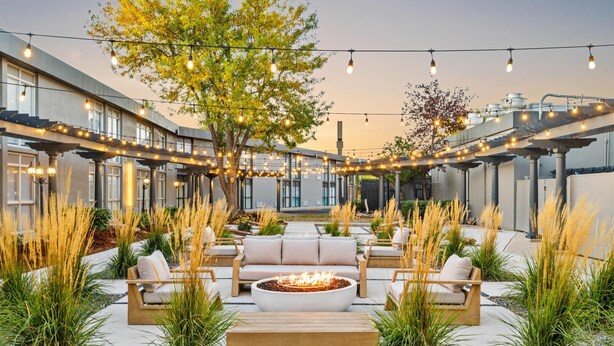An outdoor seating area with a fire pit, surrounded by sofas and chairs, under string lights.