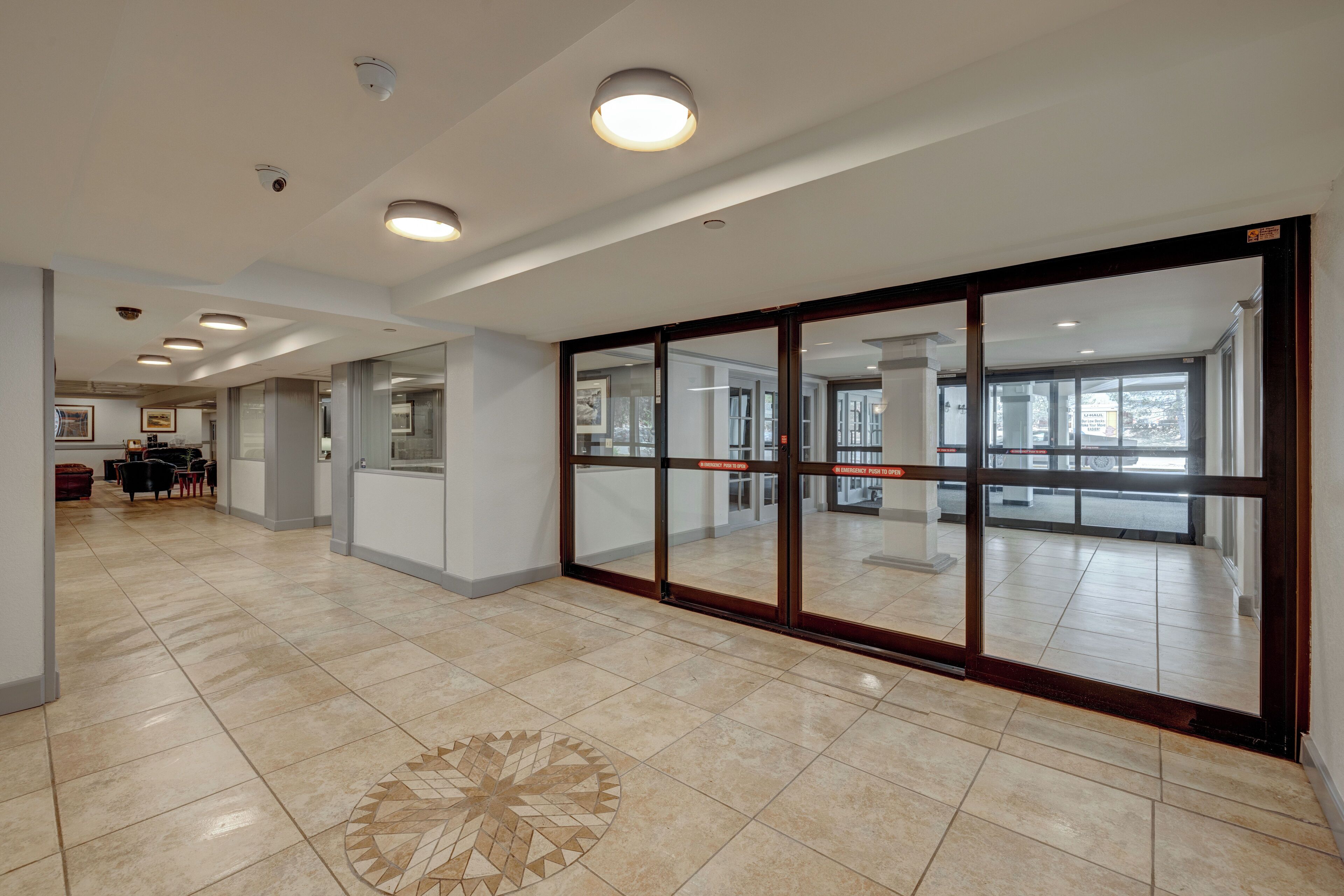 A spacious hallway with a tiled floor, a glass door leading to another area, and recessed ceiling lights.