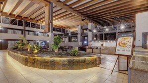A modern hotel lobby with a central fountain, seating areas, and a sign for breakfast.