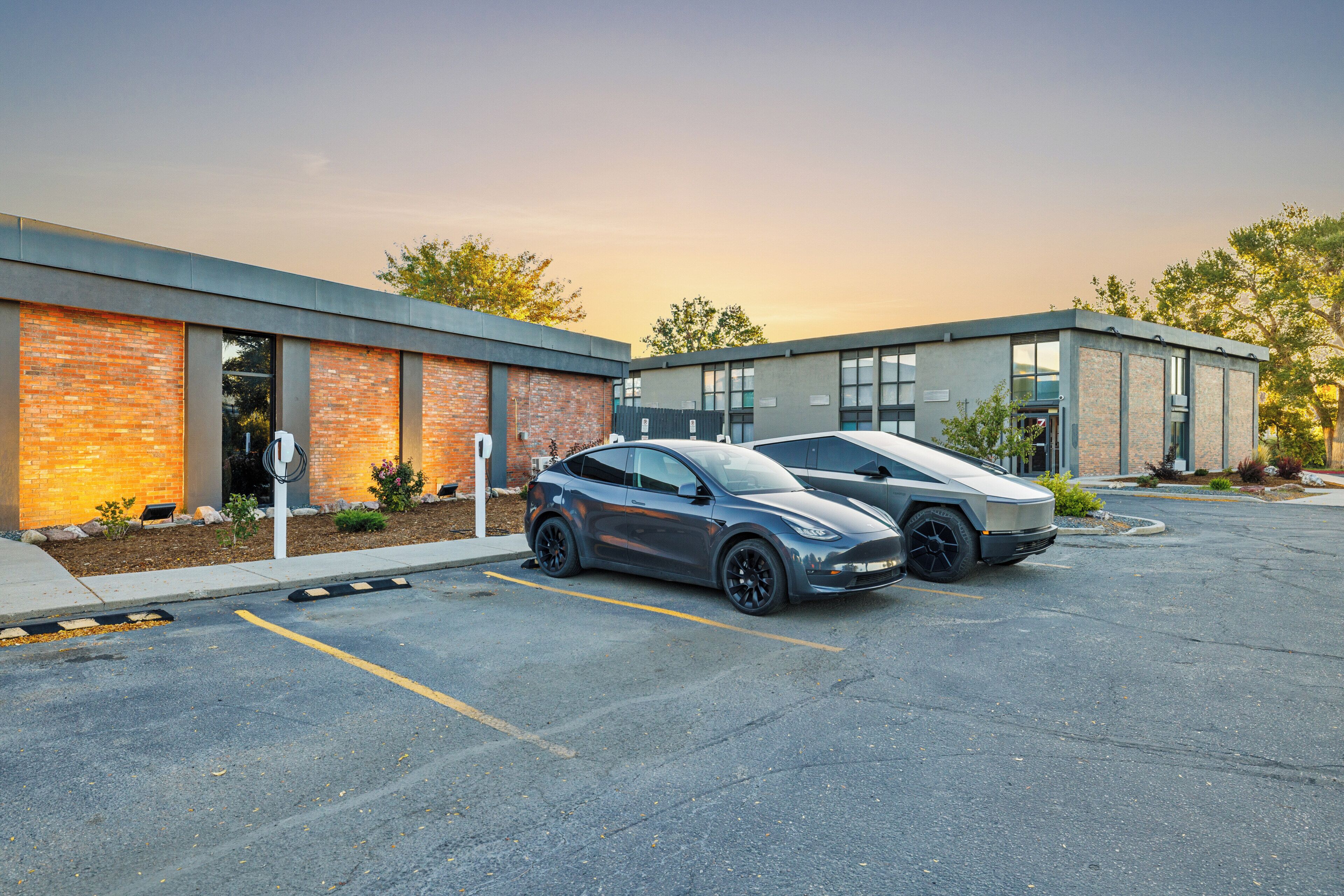 A parking lot with two cars, a building with brick and glass facade, and a clear sky.