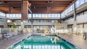 An indoor swimming pool with a tiled deck, surrounded by white railings and seating areas.