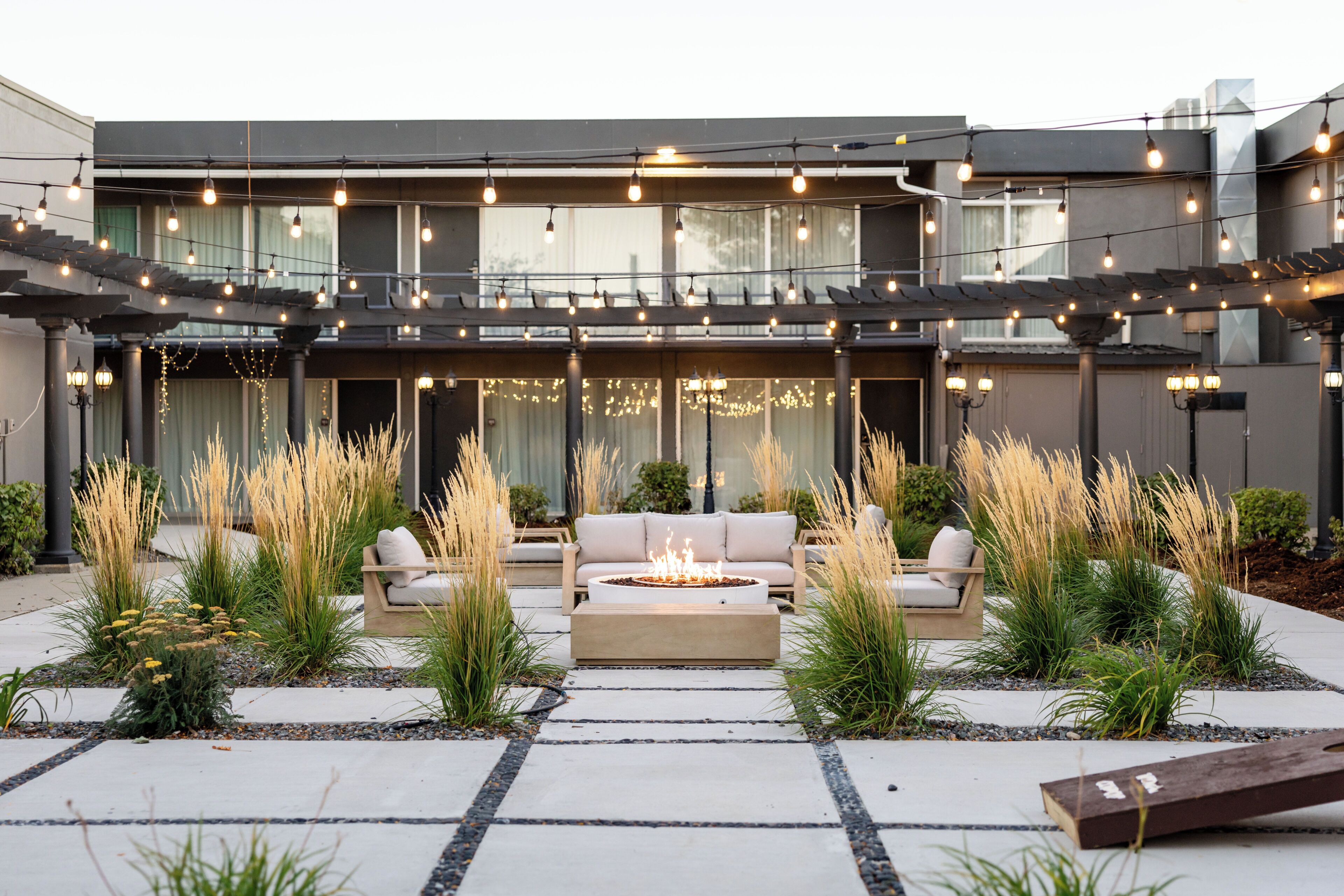 A modern outdoor patio with a fire pit, seating area, and string lights.