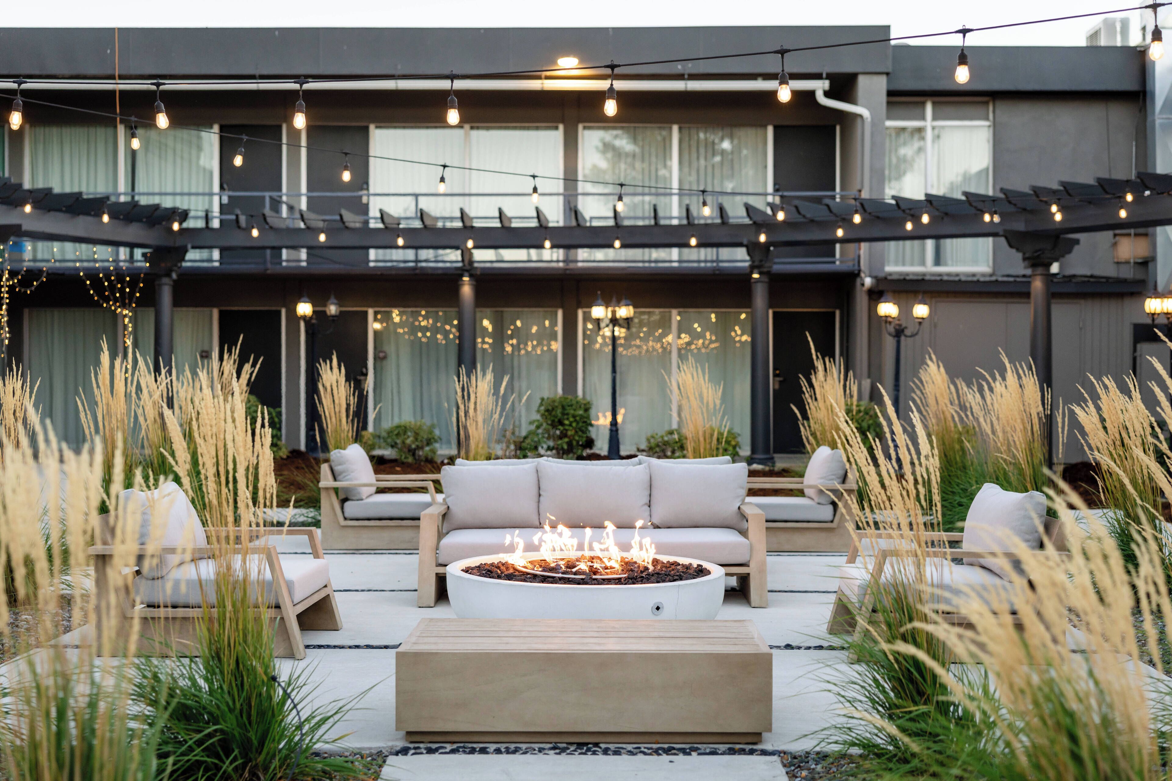 An outdoor seating area with a fire pit, lounge chairs, and a pergola with string lights.