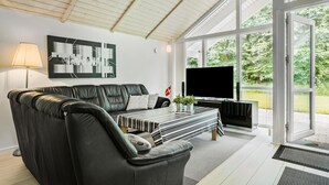 Un salon moderne avec un canapé en cuir, un téléviseur à écran plat et une grande fenêtre donnant sur un paysage verdoyant.